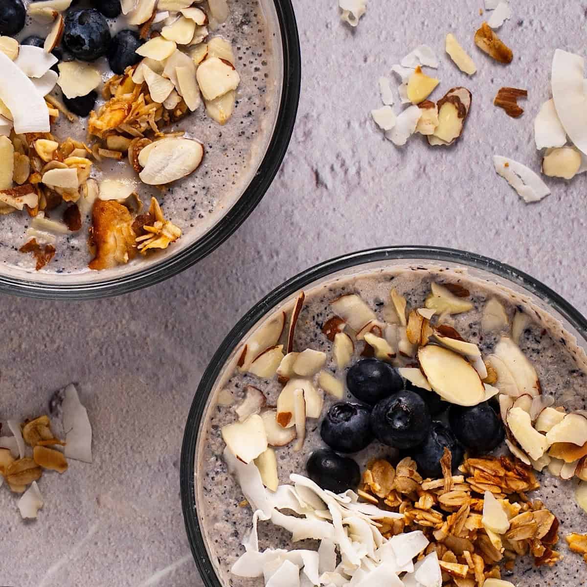Two bowls of blueberry chia pudding with granola, coconut, and almond toppings.