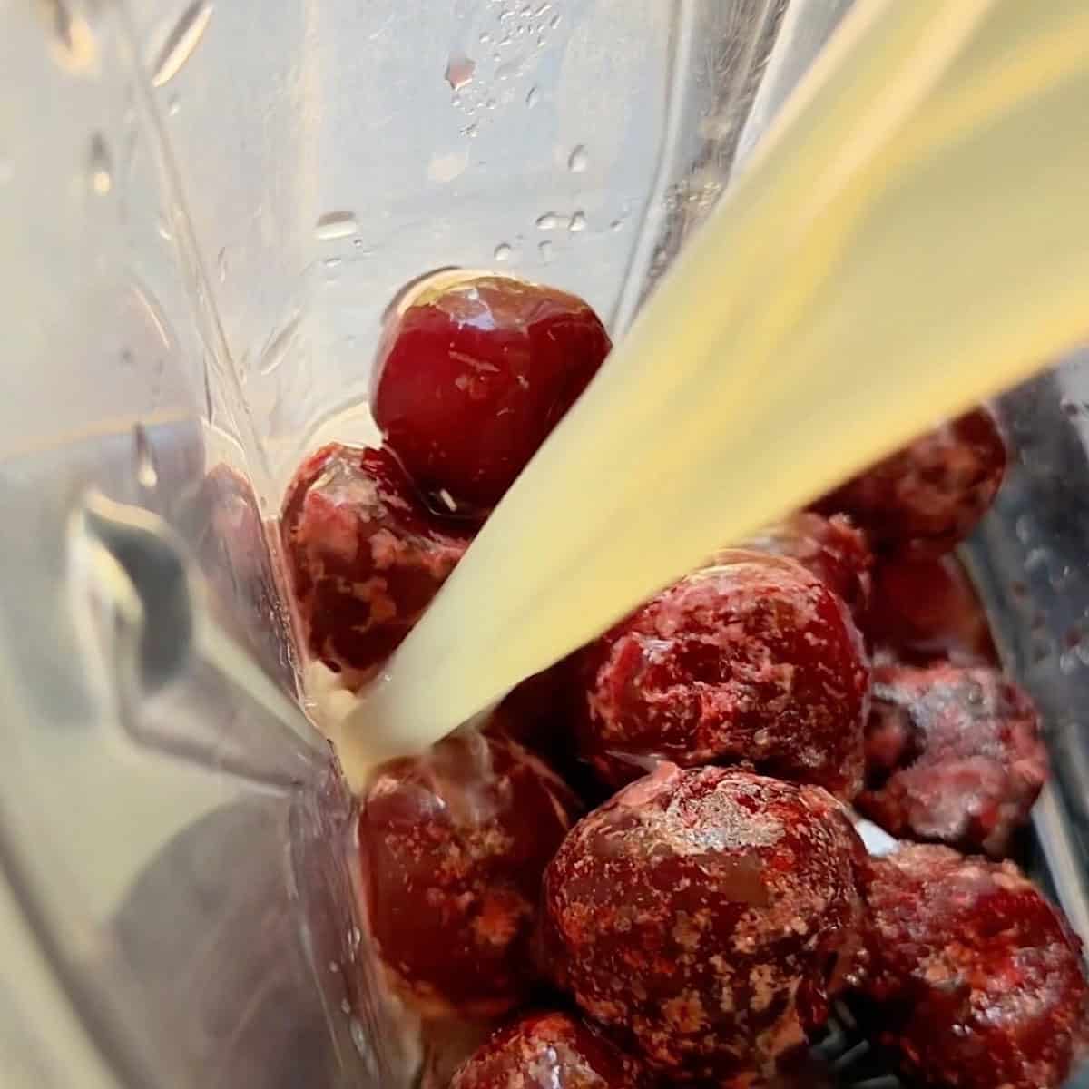 Adding fresh lime juice to frozen cherries in a blender.