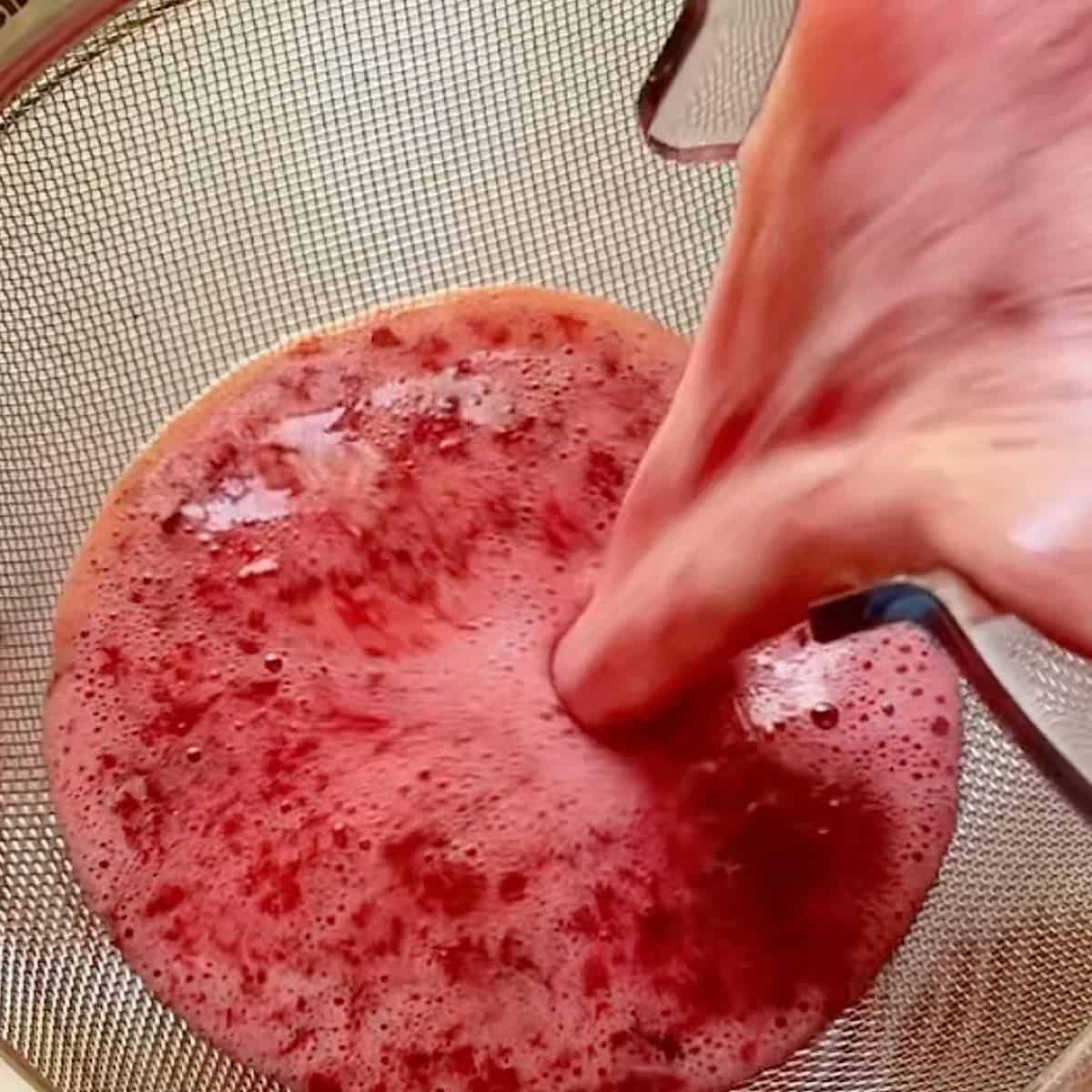 Straining the cherry lime juice through a mesh sieve.