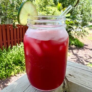 A mason jar filled with cherry limeade, ice,a lime wheel, and a glass straw.