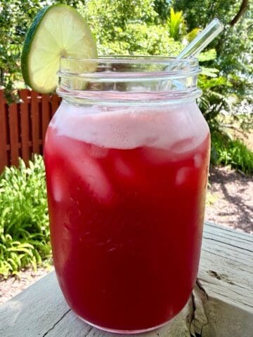 A mason jar filled with cherry limeade, ice,a lime wheel, and a glass straw.
