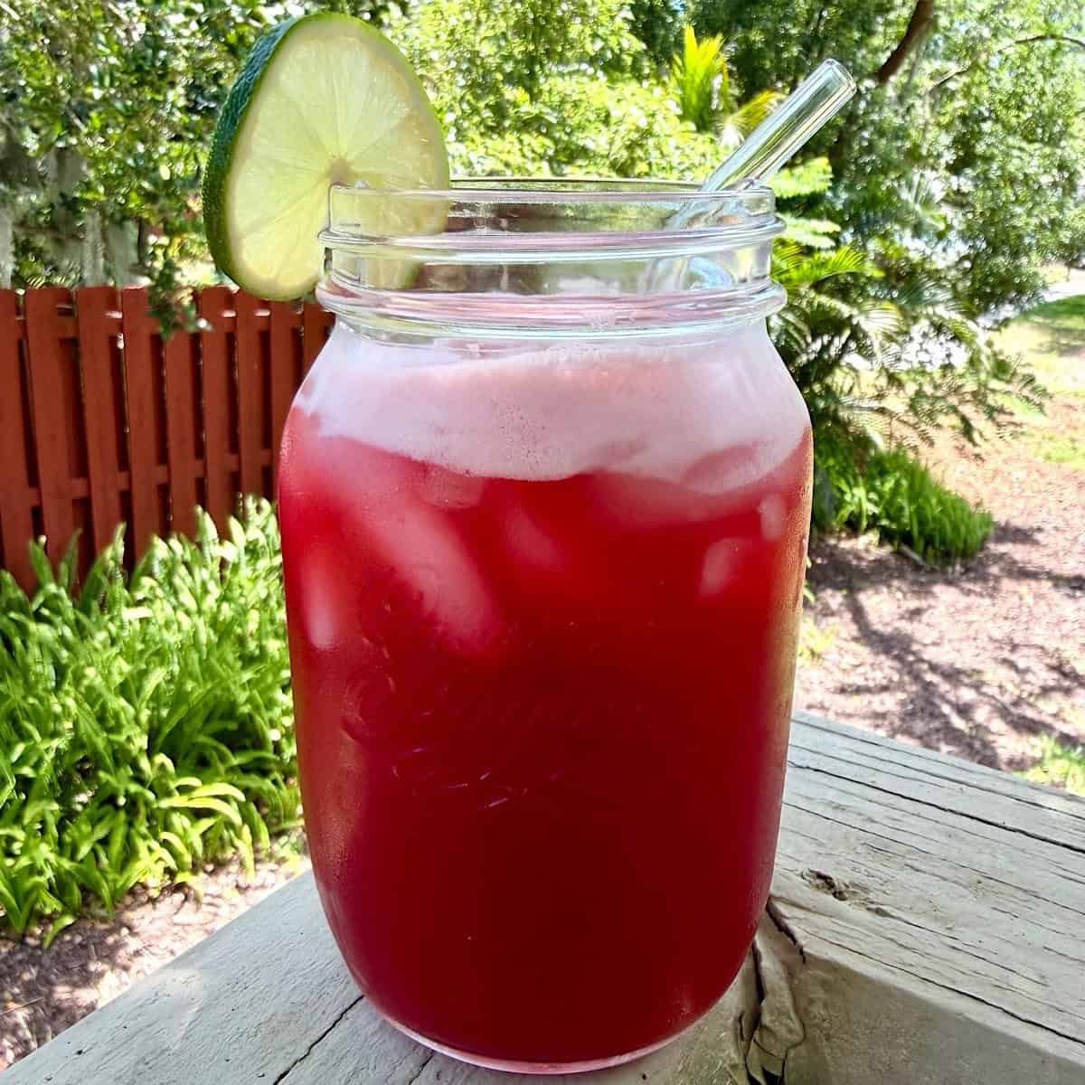 A mason jar filled with cherry limeade, ice,a lime wheel, and a glass straw.
