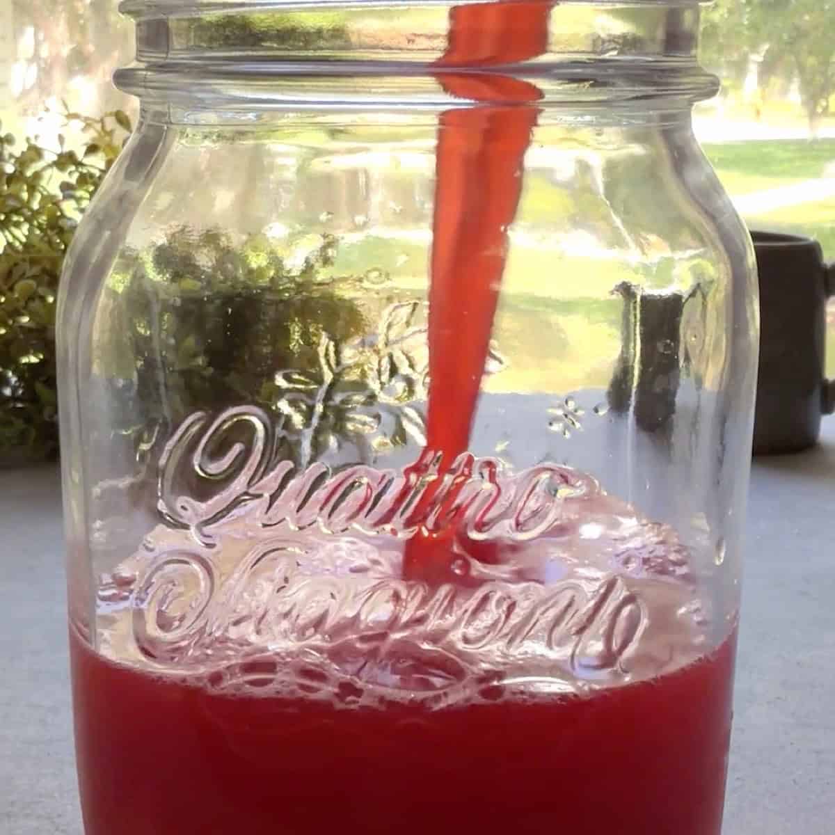 Pouring cherry limeade over a mason jar filled with ice.