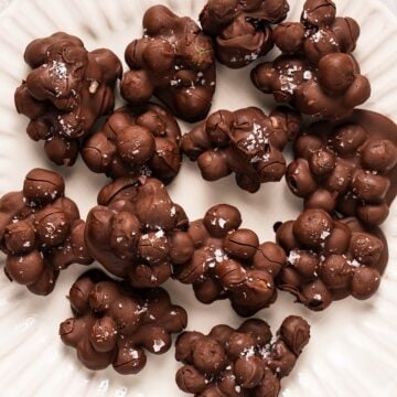 A fluted decorative plate with frozen chocolate covered blueberries clustered together and topped with flaky salt.