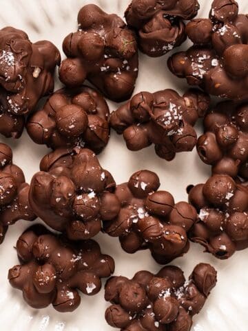 A fluted decorative plate with frozen chocolate covered blueberries clustered together and topped with flaky salt.