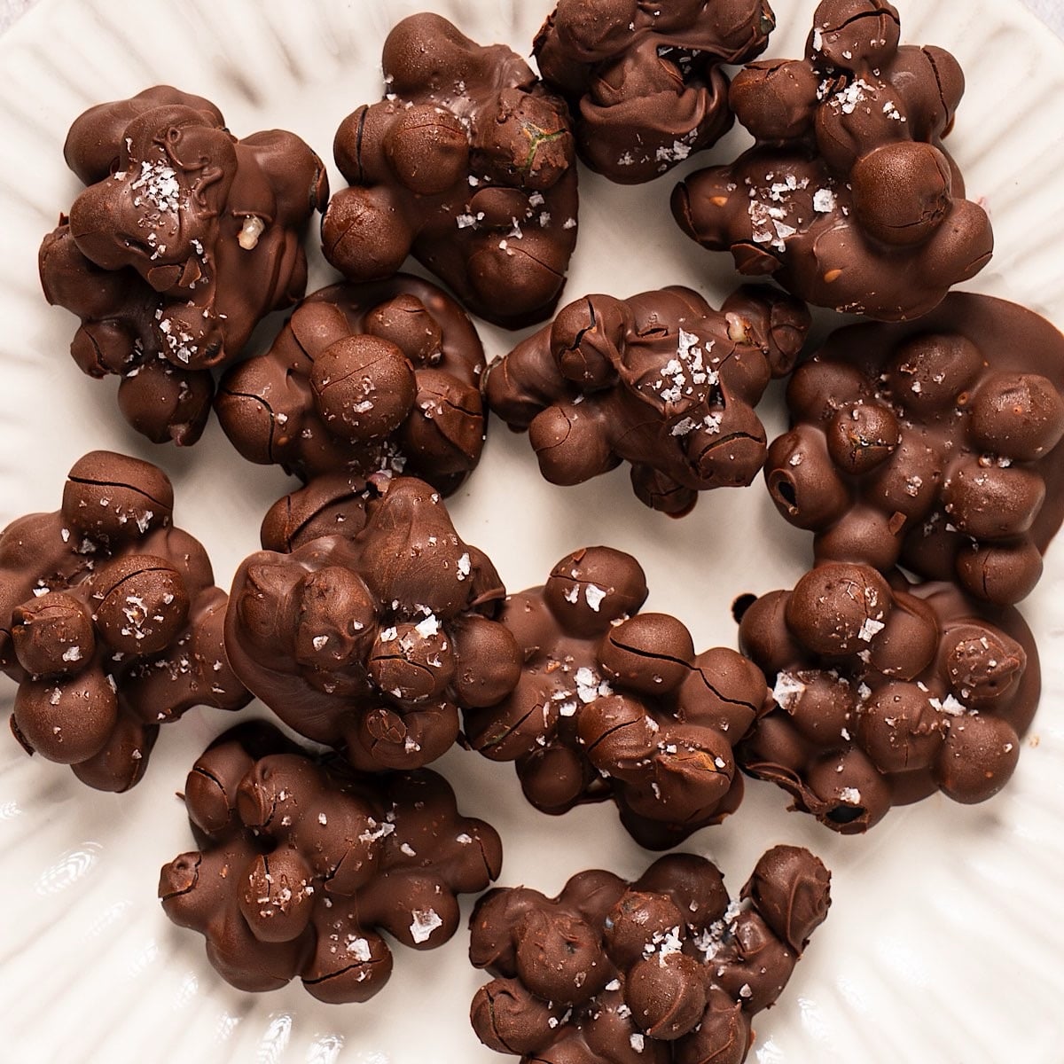 A fluted decorative plate with frozen chocolate covered blueberries clustered together and topped with flaky salt.
