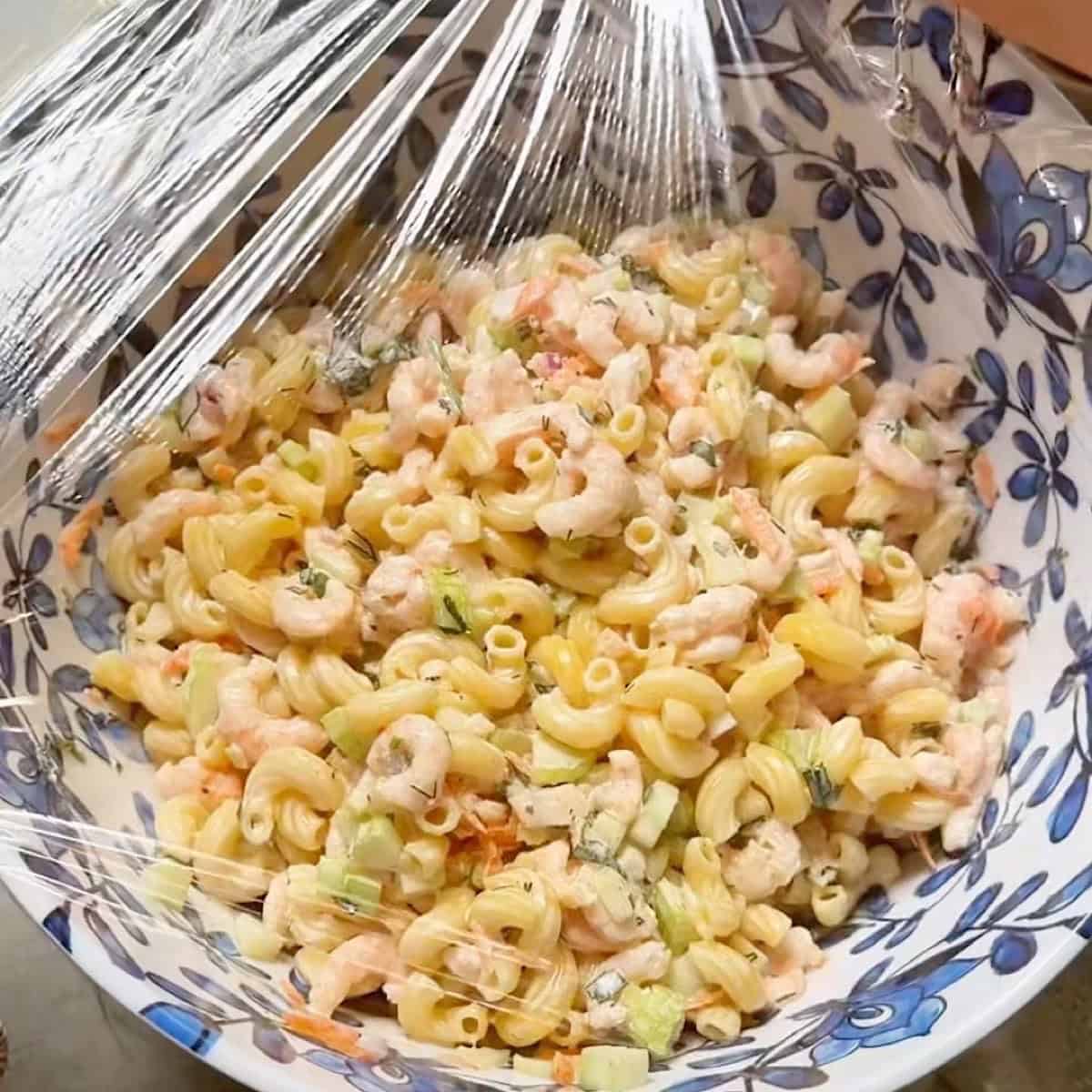 Covering the macaroni shrimp salad with plastic wrap.