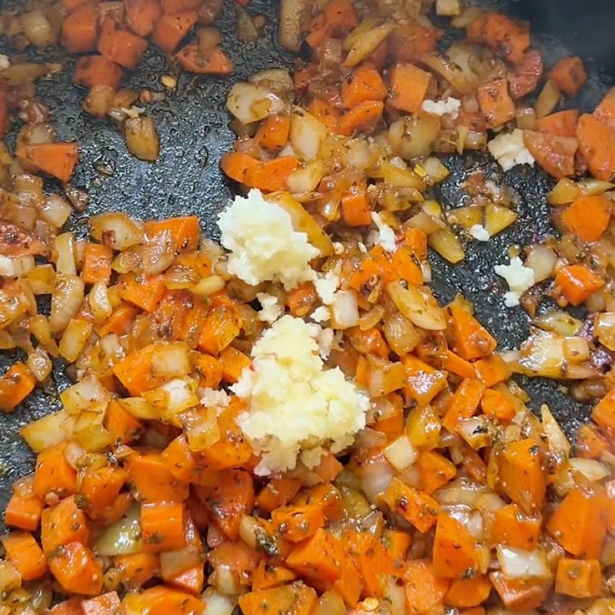 Adding garlic and tomato paste to the deglazed vegetables with white wine.