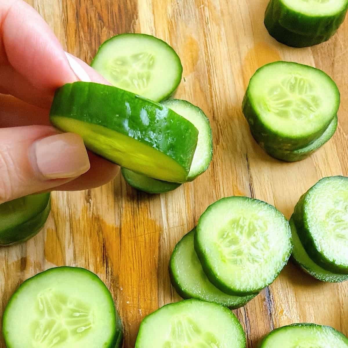 Holding a ยผ inch piece of sliced cucumber over a cutting board of remaining sliced cucumbers.
