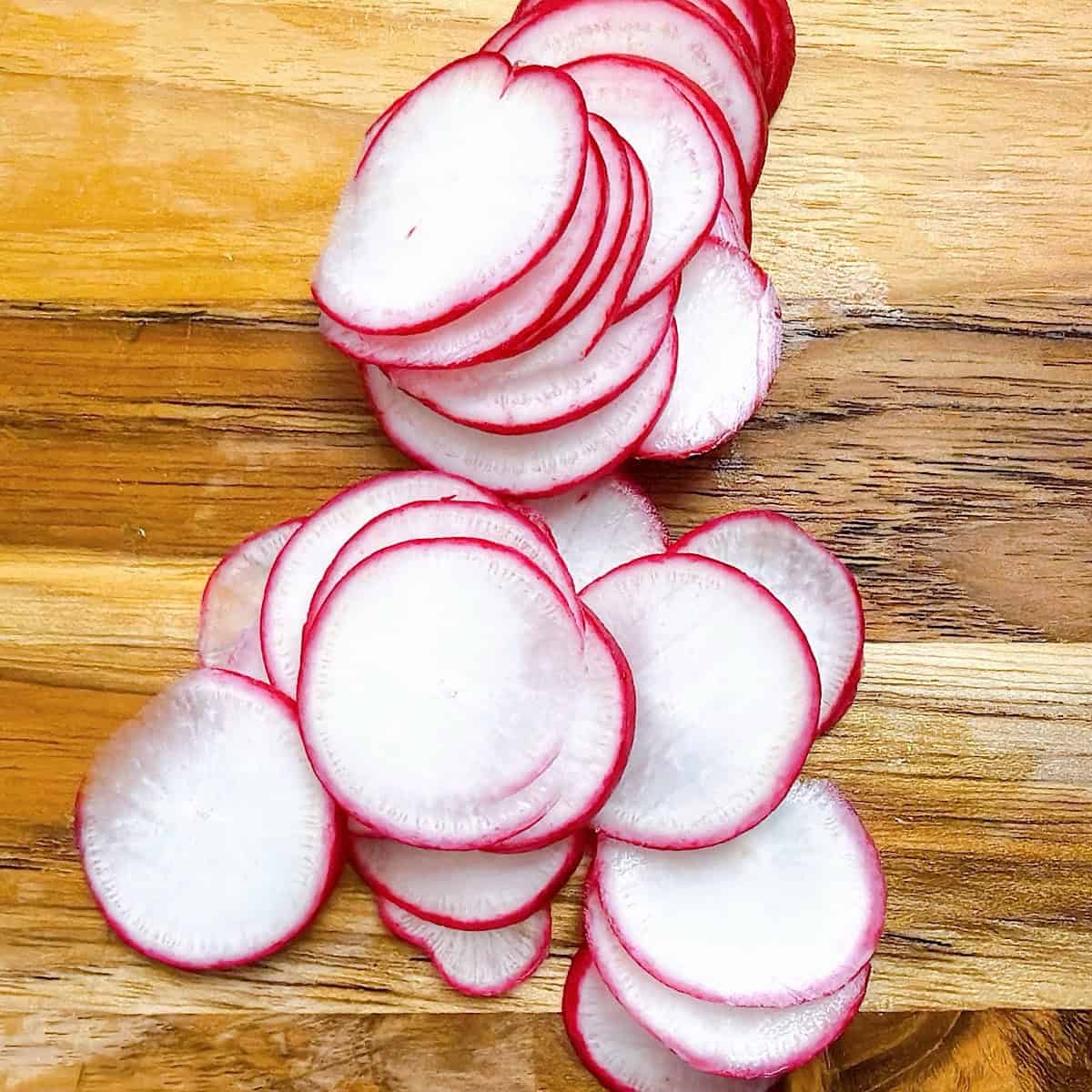 Paper thin slices radishes on a cutting board.