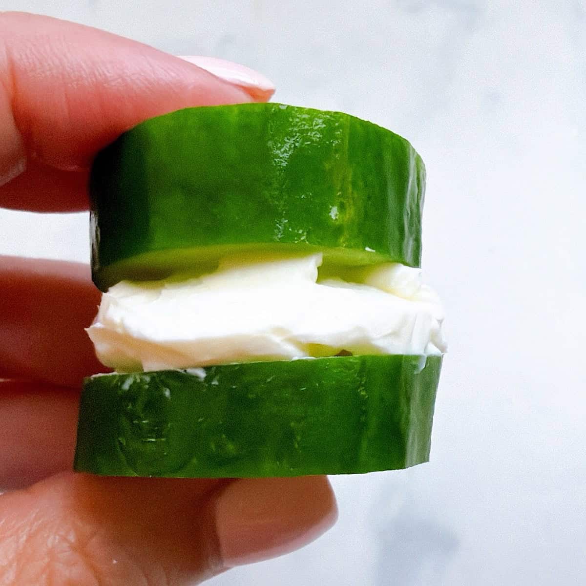 Holding a cucumber stack with whipped cream cheese in the middle.