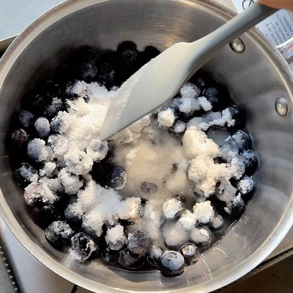 Stirring blueberries with sugar and water in a saucepan.