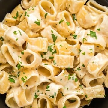 Homemade alfredo sauce with heavy whipping cream coating pasta in a black bowl with garnish.
