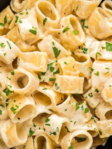 Homemade alfredo sauce with heavy whipping cream coating pasta in a black bowl with garnish.