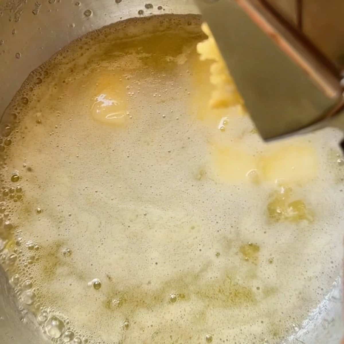 Using a garlic press to squeeze garlic into melted butter.