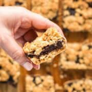 Holding a homemade fig oatmeal bar over remaining bars to show the fig filling.