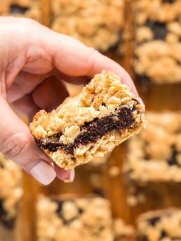 Holding a homemade fig oatmeal bar over remaining bars to show the fig filling.