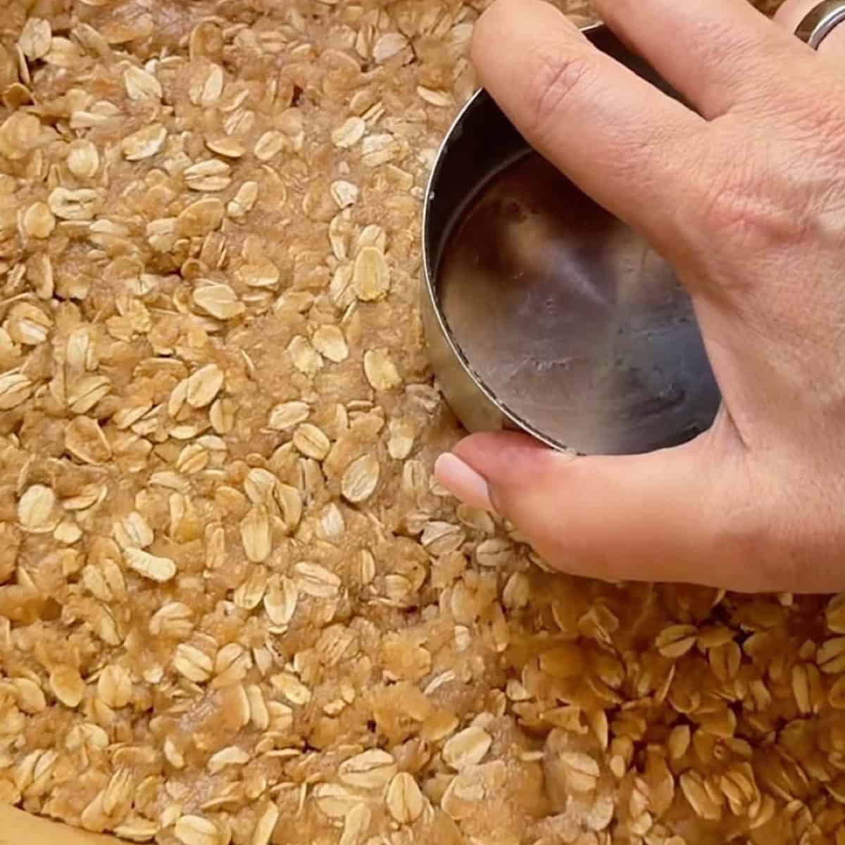 Pressing the crumb crust into the baking pan with a measuring cup.