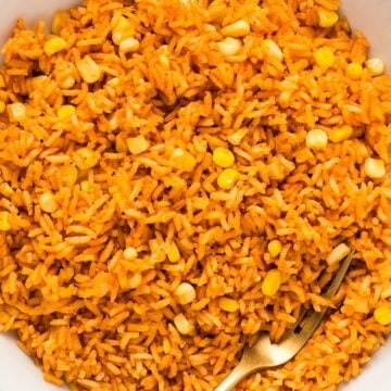 Mexican rice with corn in a white bowl with a gold fork showing separation of grains.