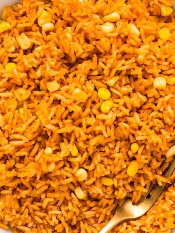 Mexican rice with corn in a white bowl with a gold fork showing separation of grains.