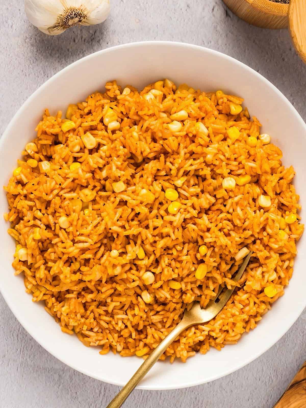 Mexican rice with corn plated next to linen, wooden bowl, and wooden spoon.