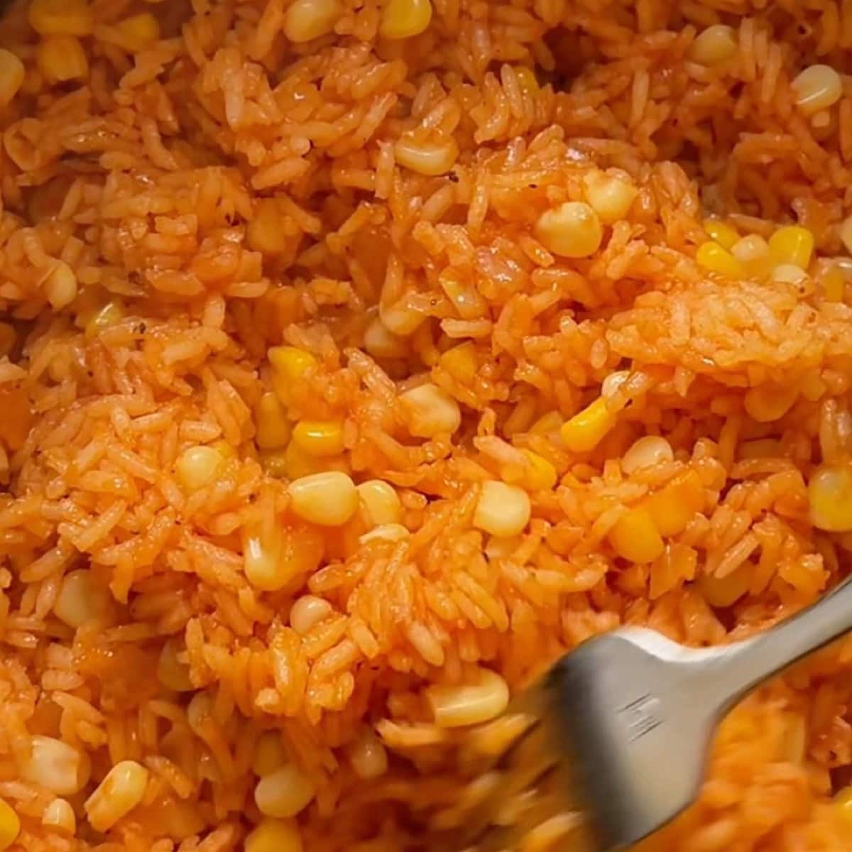 Fluffing the Mexican rice with corn with a fork after resting.