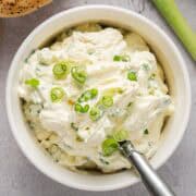 Scallion cream cheese in a bowl plated with scallion garnish and decorative serving spoon.