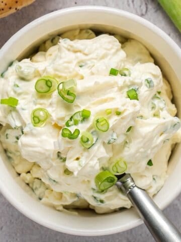Scallion cream cheese in a bowl plated with scallion garnish and decorative serving spoon.