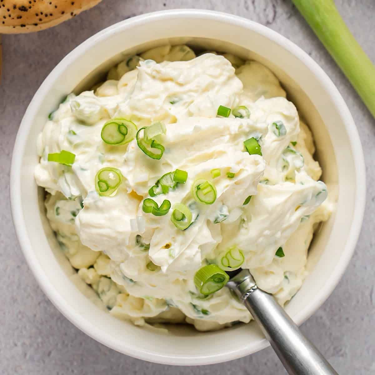 Scallion cream cheese in a bowl plated with scallion garnish and decorative serving spoon.