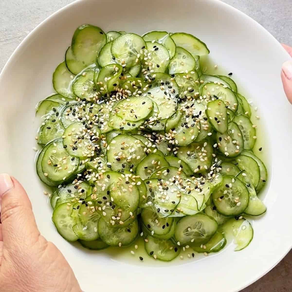 Holding a sunomono salad garnished with sesame seeds in a shallow white bowl.