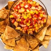 Fruit salsa in glass serving bowl with cinnamon tortilla chips arranged around the edges.