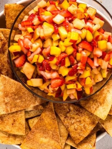 Fruit salsa in glass serving bowl with cinnamon tortilla chips arranged around the edges.
