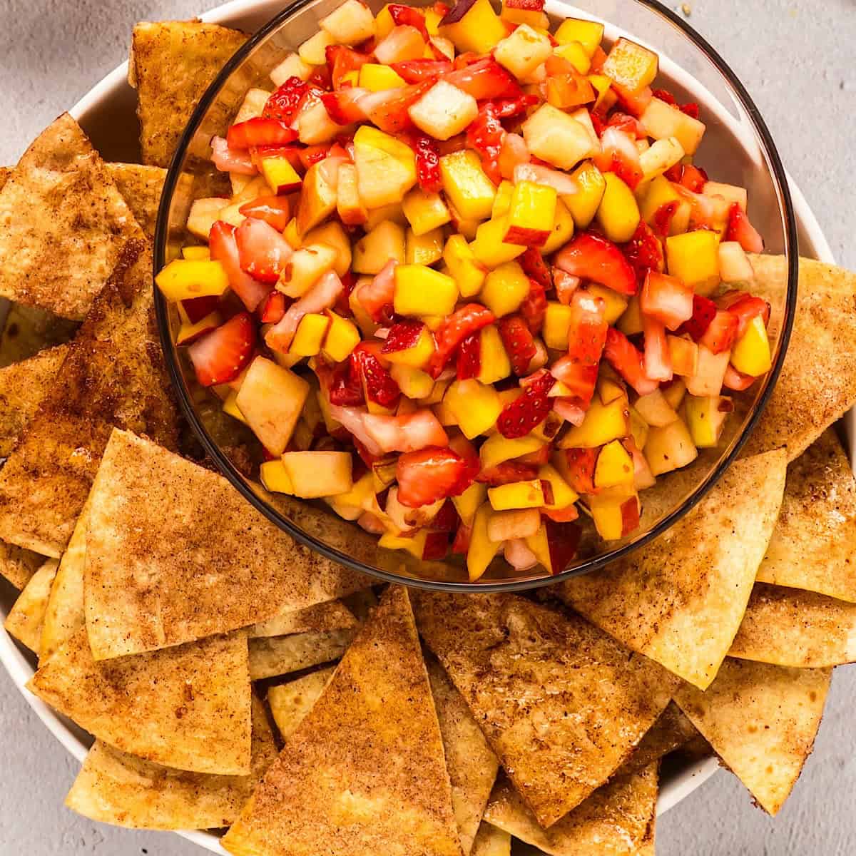 Fruit salsa in glass serving bowl with cinnamon tortilla chips arranged around the edges.