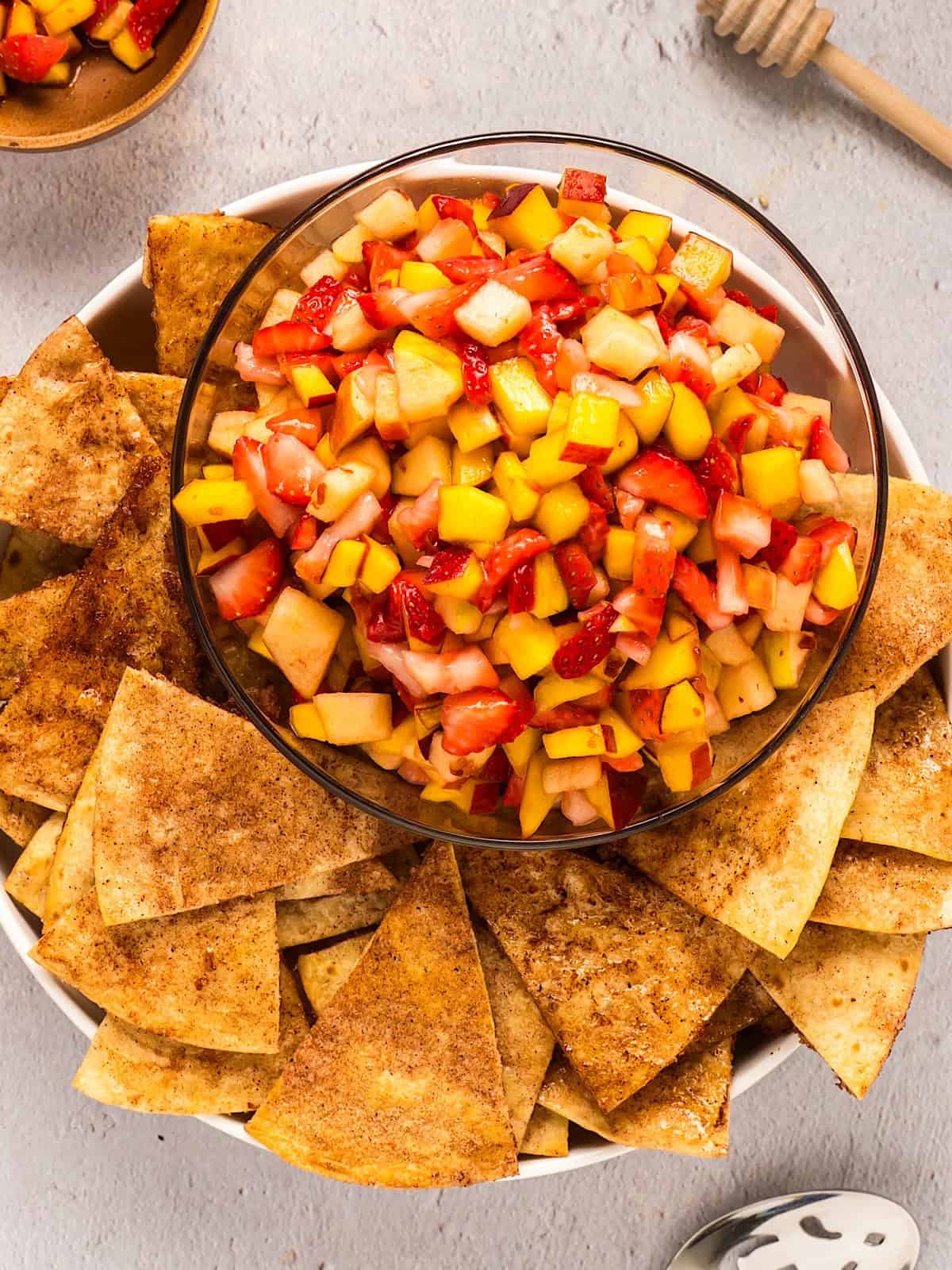Fruit salsa in glass serving bowl with cinnamon tortilla chips arranged around the edges.