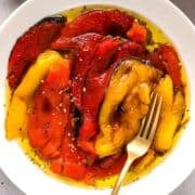 Marinated Italian roasted peppers in a white bowl with a gold fork for serving.