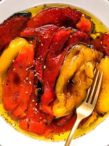 Marinated Italian roasted peppers in a white bowl with a gold fork for serving.