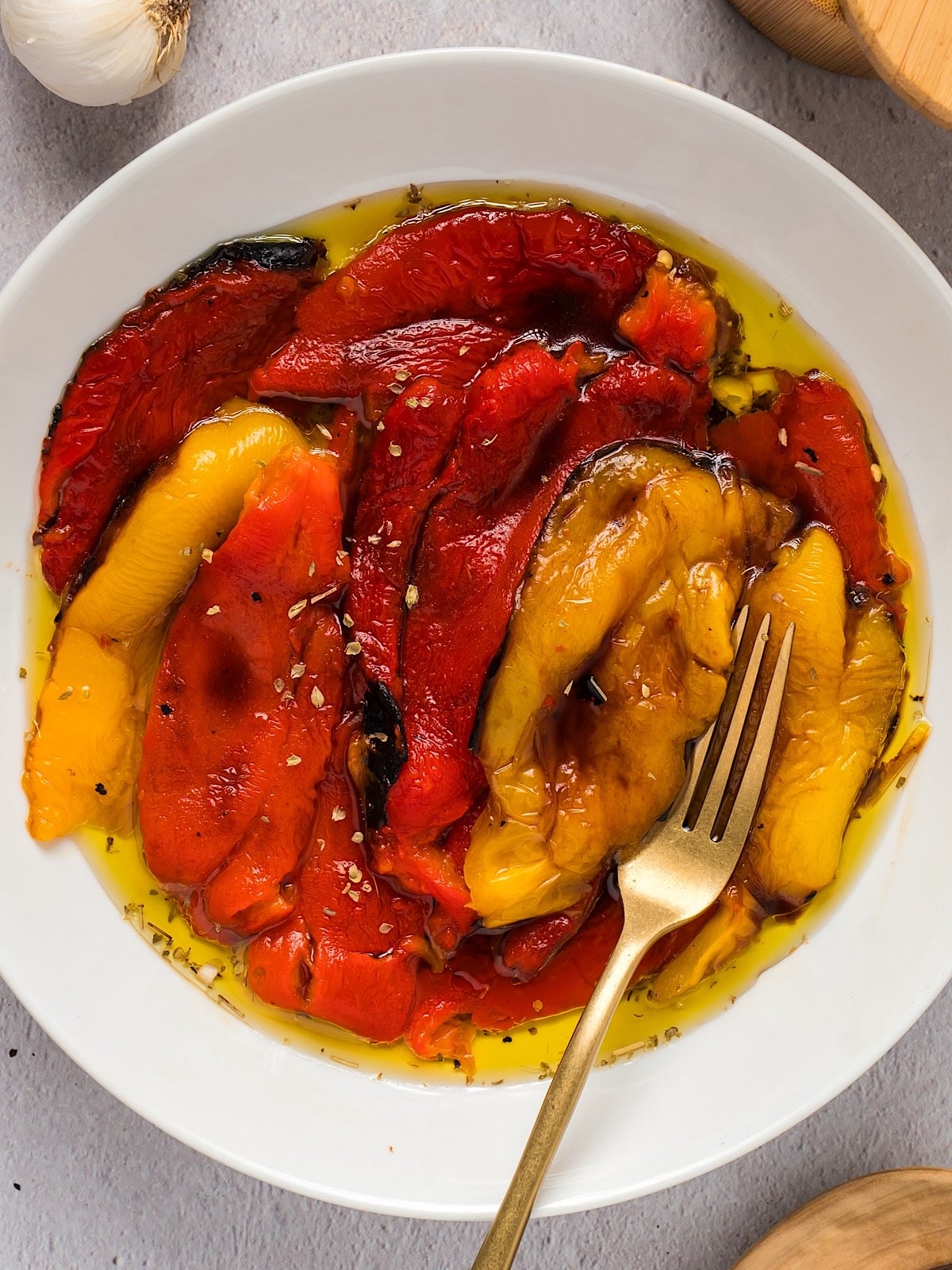 Italian roasted peppers marinating in olive oil and garlic with a gold folk for serving.