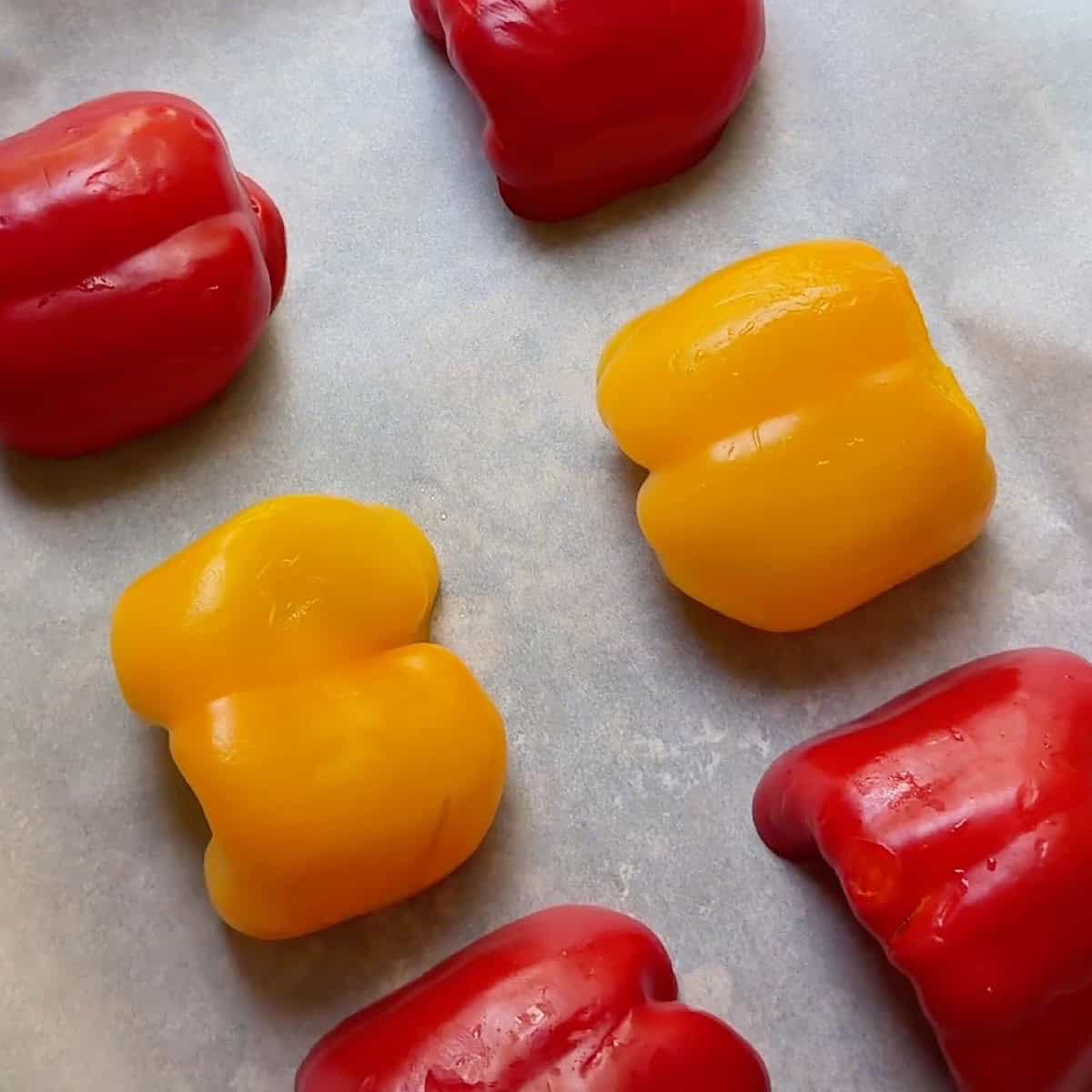 Halved yellow and red bell pepper on a sheet pan with parchment.