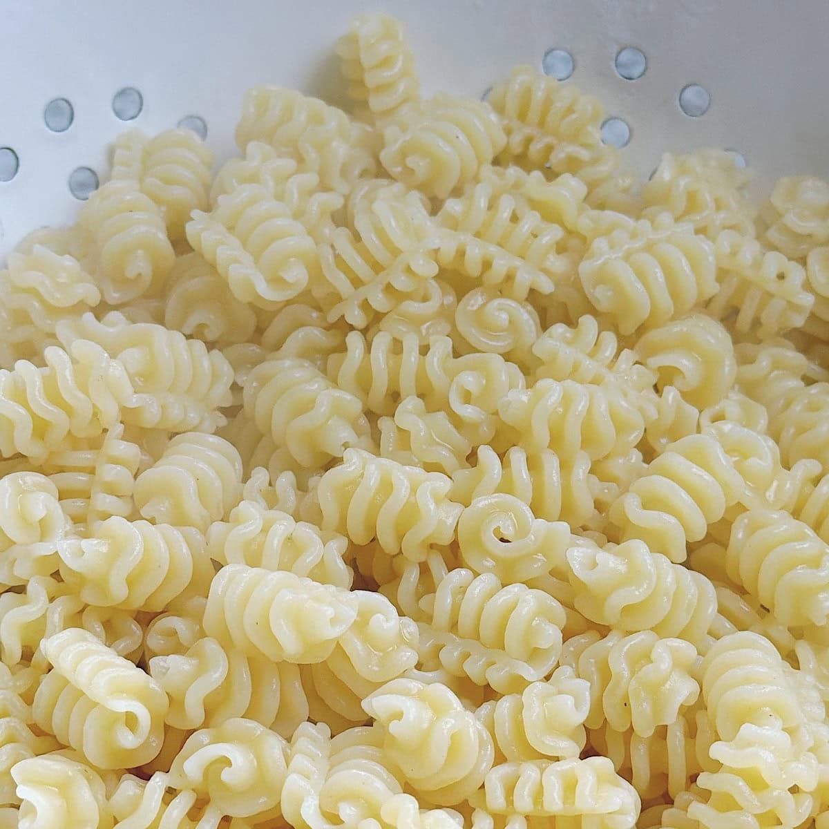 Pasta draining in a colander with steam rising up.