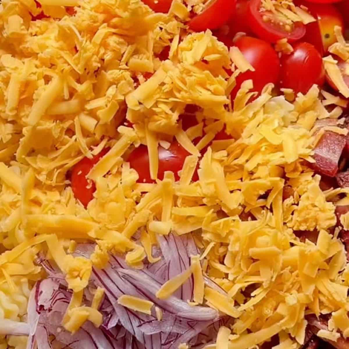 Preparing the salad base with pasta, bacon, tomato, and red onion.
