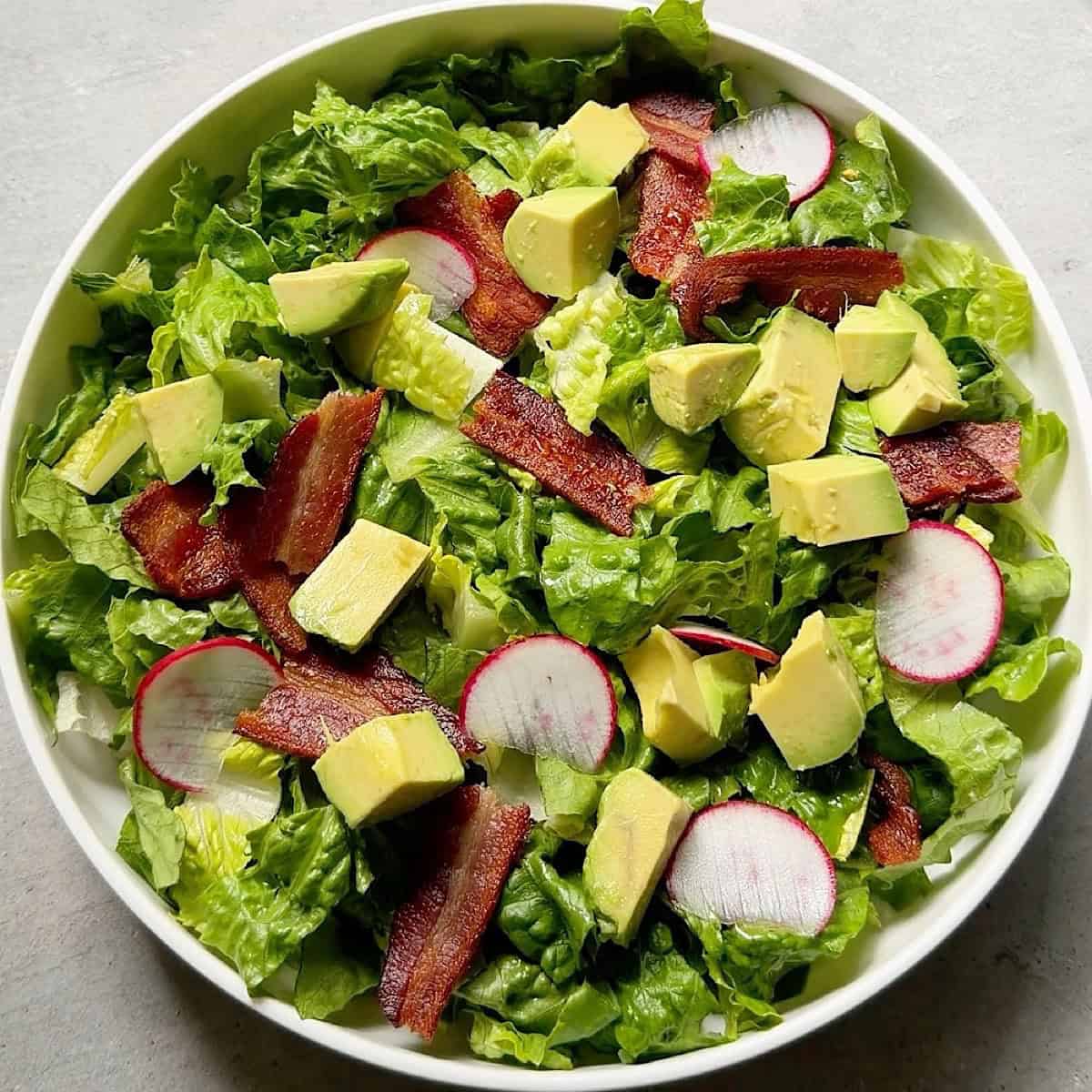Adding bacon, radish, and avocado toppings to the breakfast salad.