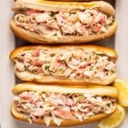 Crab salad sandwiches on a platter with lemon wedges.