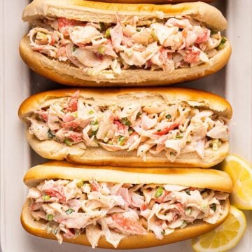 Crab salad sandwiches on a platter with lemon wedges.