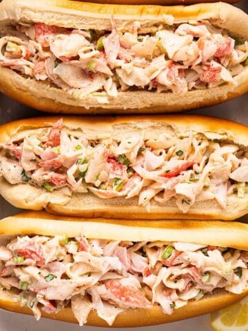 Crab salad sandwiches on a platter with lemon wedges.