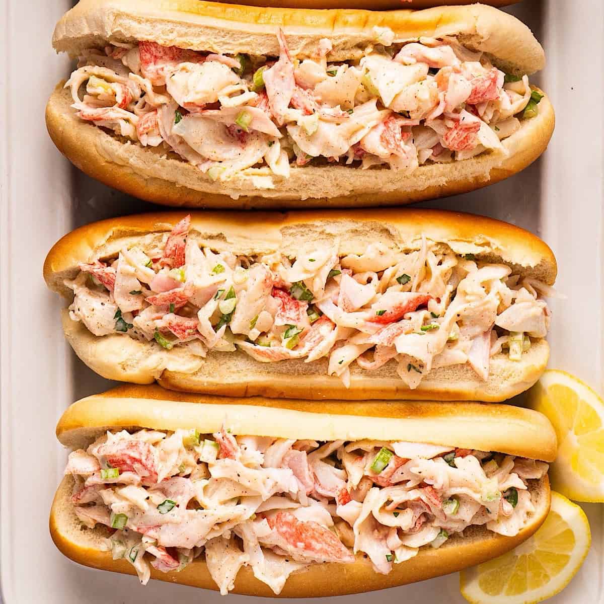 Crab salad sandwiches on a platter with lemon wedges.