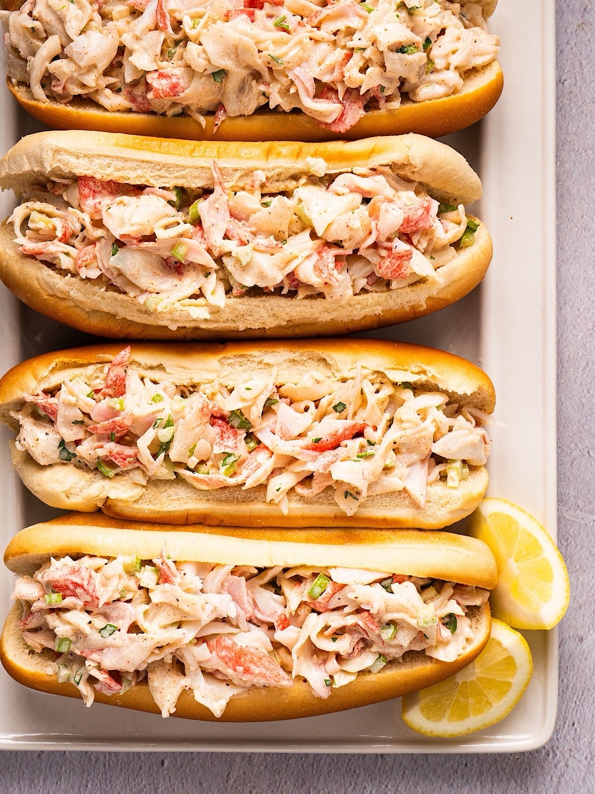 Four crab salad sandwiches on a platter with lemon.