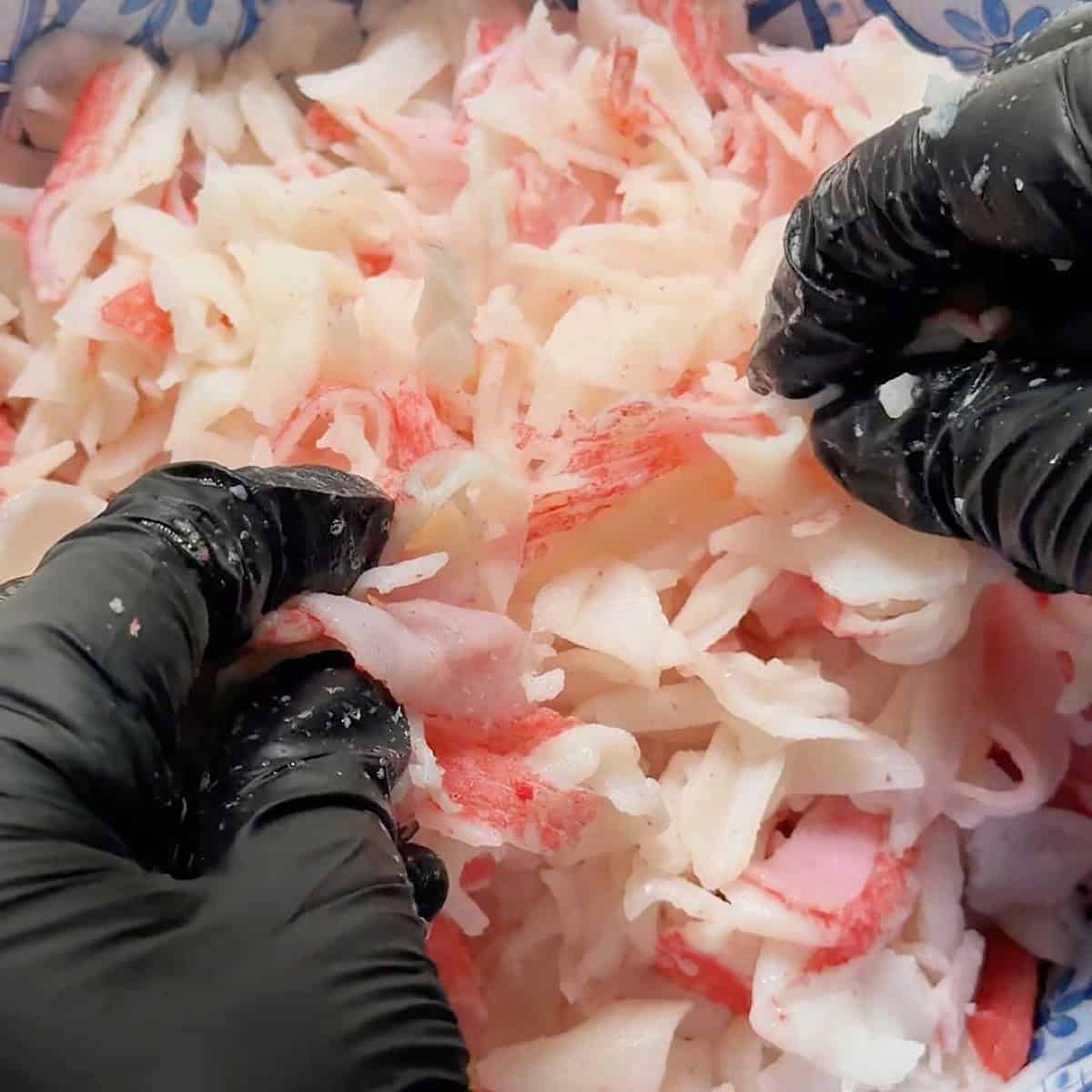 Shredding the imitation crab meat by hand in a mixing bowl.