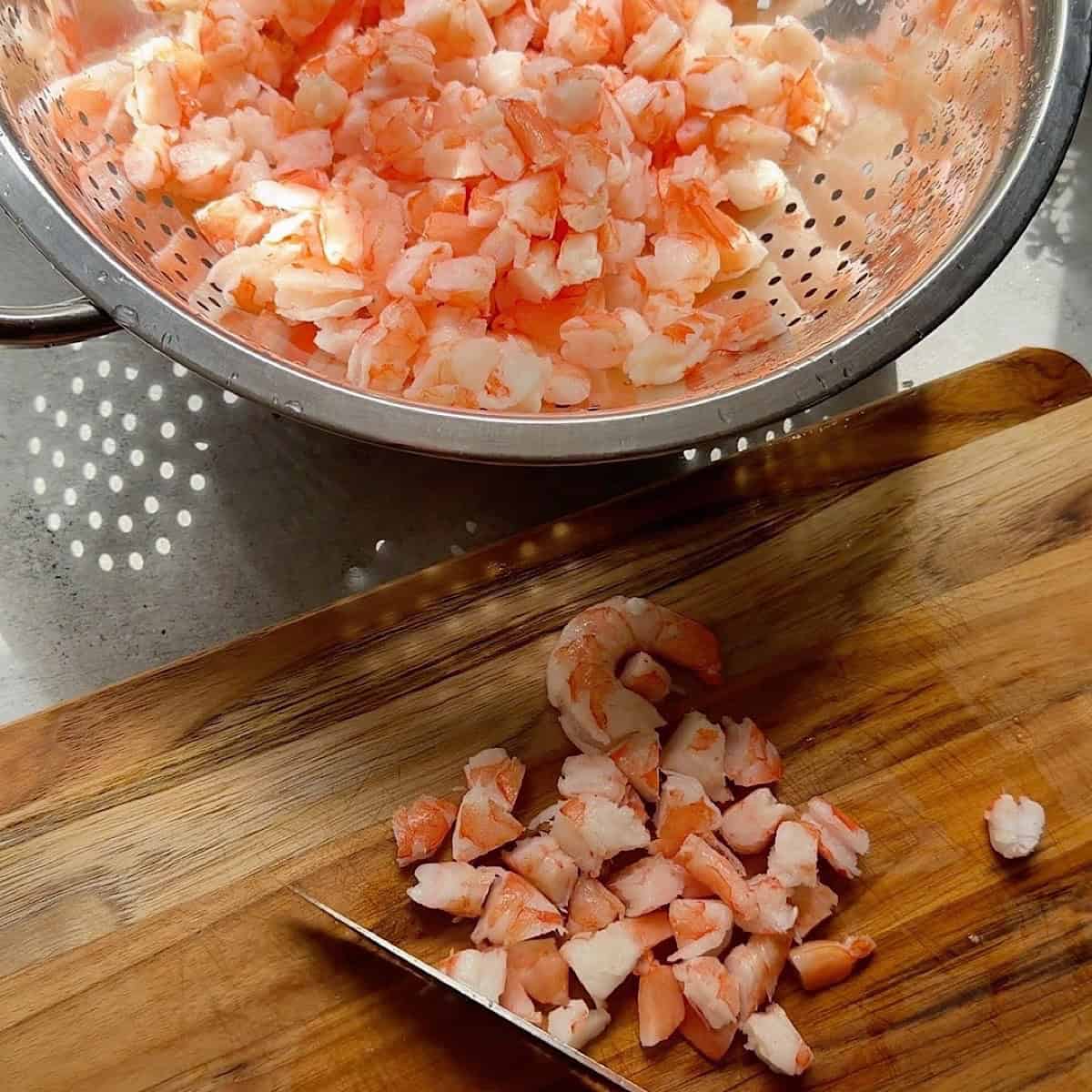 Roughly chopping shrimp on a cutting board near colander.