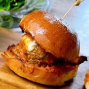 One meatball slider on a serving tray with melty cheese and sauce showing.