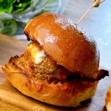 One meatball slider on a serving tray with melty cheese and sauce showing.